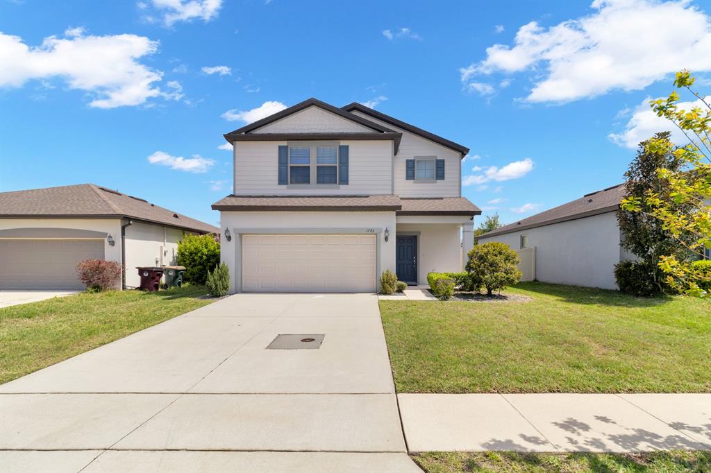 A two-story suburban house with a beige exterior, a two-car garage, and a concrete driveway — 1793 CAYMAN COVE CIRCLE, ST CLOUD, FL