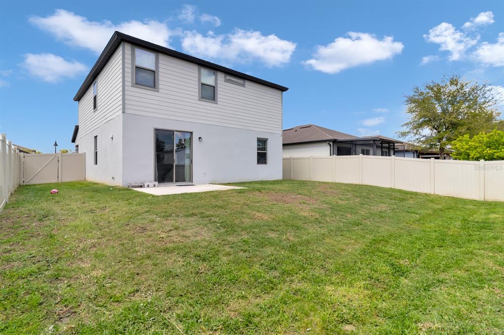 The backyard of a two-story house features a concrete patio and a vinyl privacy fence — 1793 CAYMAN COVE CIRCLE, ST CLOUD, FL