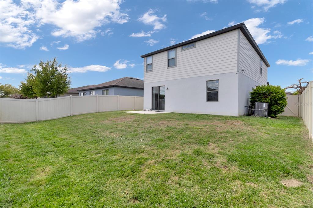 The backyard of a two-story house features a small concrete patio and a vinyl fence — 1793 CAYMAN COVE CIRCLE, ST CLOUD, FL