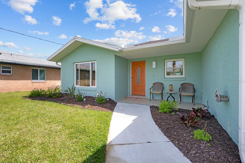 A light green house exterior features an orange front door, a concrete walkway, and landscaping — 1946 N DAYTONA AVENUE, FLAGLER BEACH, FL