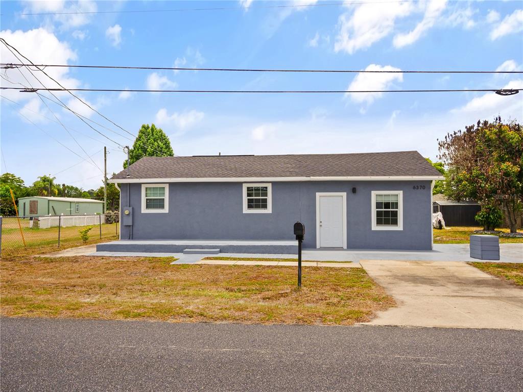 A gray, single-story house features a white door, white-trimmed windows, and a concrete patio — 6370 BASS HIGHWAY, ST CLOUD, FL