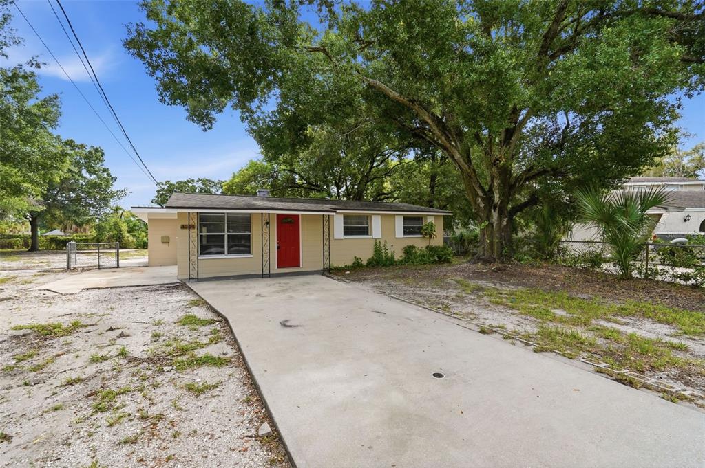 A single-story house with a red front door, concrete driveway, and large trees in front — 3209 N 45TH STREET, TAMPA, FL