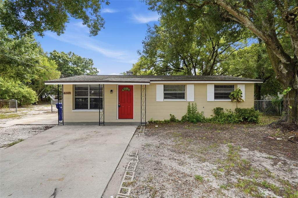 A single-story house with tan siding, a red front door, and a concrete driveway — 3209 N 45TH STREET, TAMPA, FL