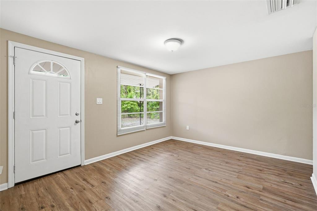 An empty room features beige walls, wood-look flooring, a white front door, and a window — 3209 N 45TH STREET, TAMPA, FL