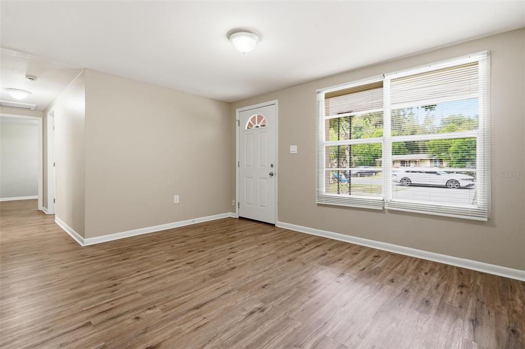 An empty room with light wood-look flooring, beige walls, a white front door, and windows — 3209 N 45TH STREET, TAMPA, FL