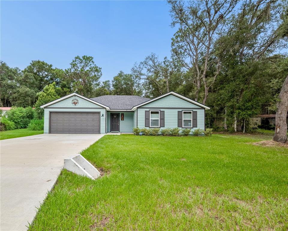 A single-story house with light green siding, a two-car garage, and a concrete driveway — 111 BREEZEWAY AVENUE, SATSUMA, FL