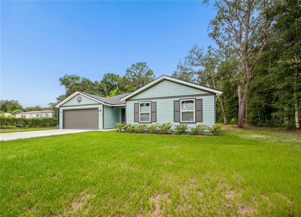 A light blue single-story house with a two-car garage and dark shutters on the windows — 111 BREEZEWAY AVENUE, SATSUMA, FL