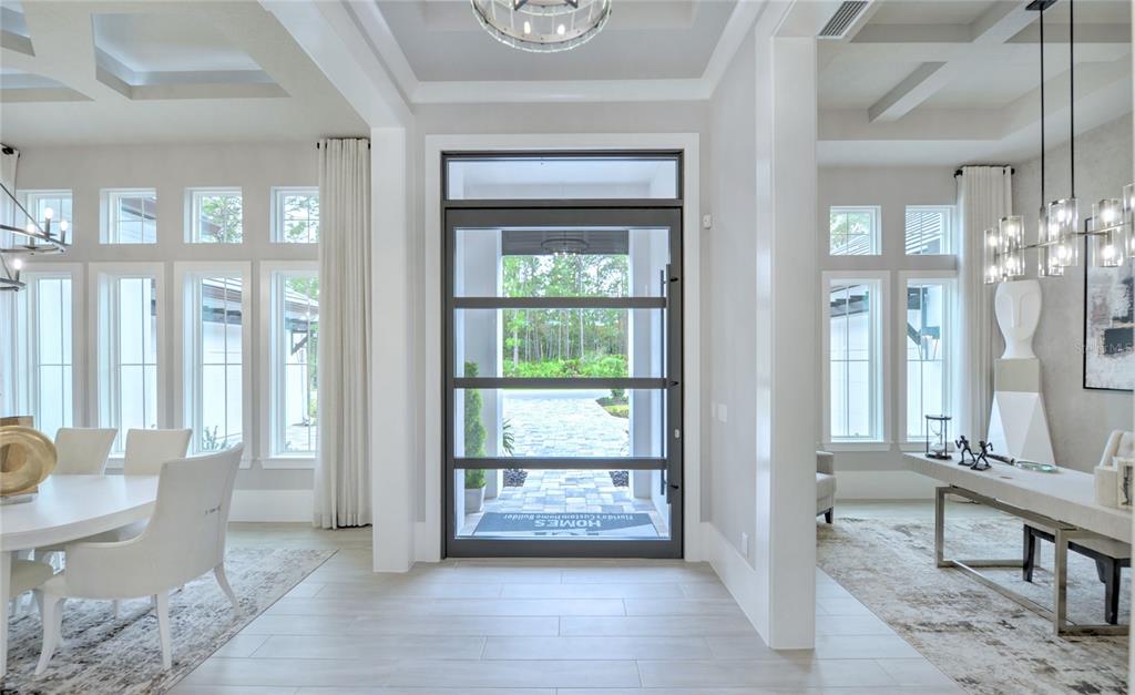 A bright foyer features a modern glass-paneled front door, light tile flooring, and coffered ceilings — 1009 SUDBURY LANE, ORMOND BEACH, FL