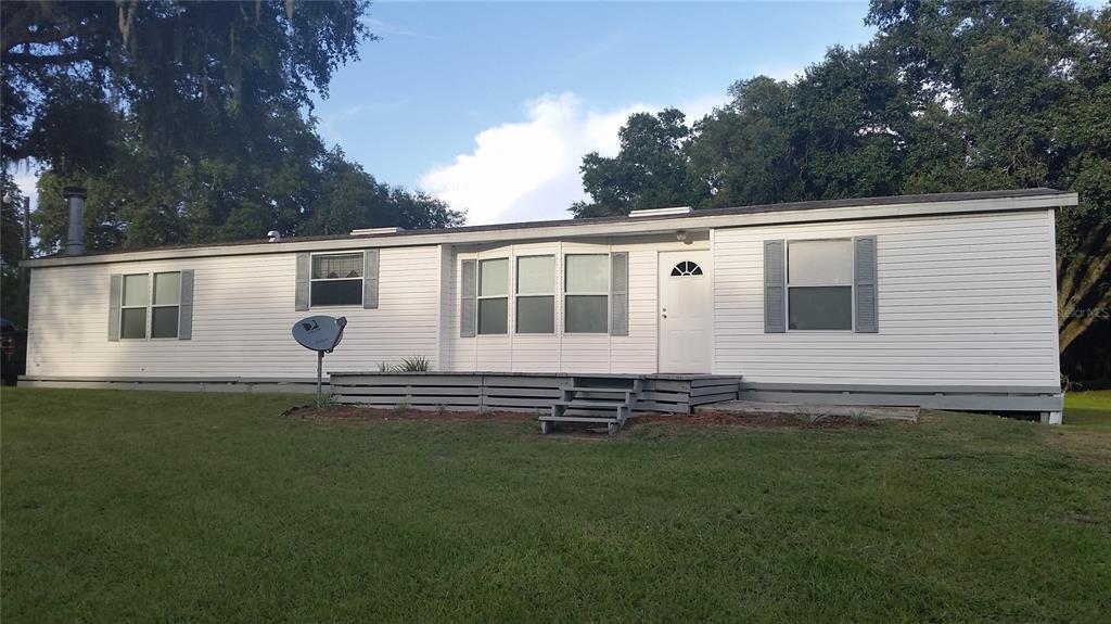 A single-story white mobile home with a front deck and satellite dish on a lawn — 30340 BAYLOR LANE, WESLEY CHAPEL, FL