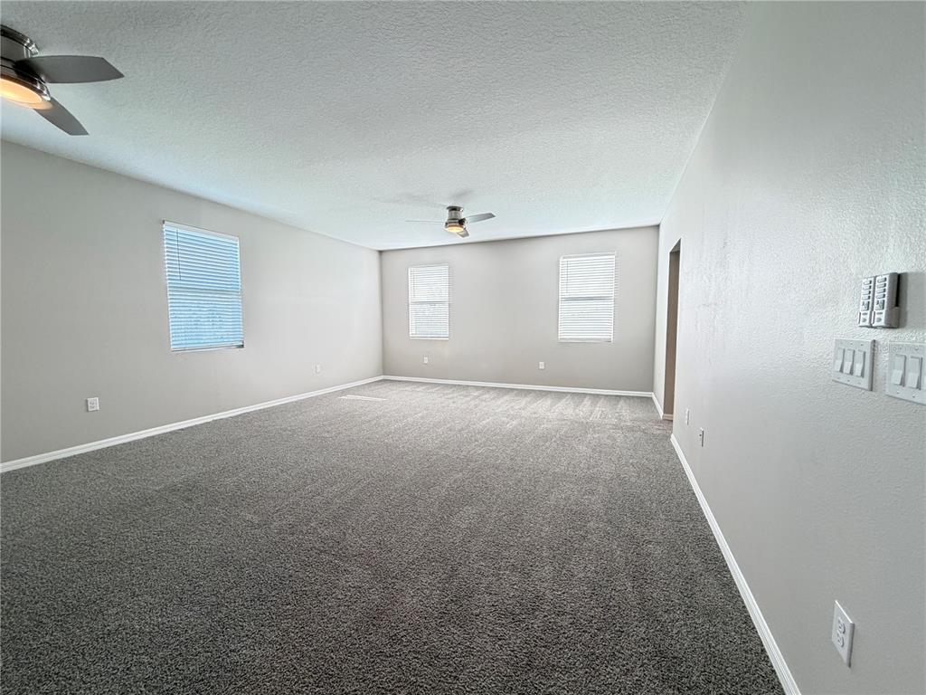 An empty room with gray carpet, light gray walls, two ceiling fans, and three windows — 860 BAY BRIDGE CIRCLE, APOPKA, FL