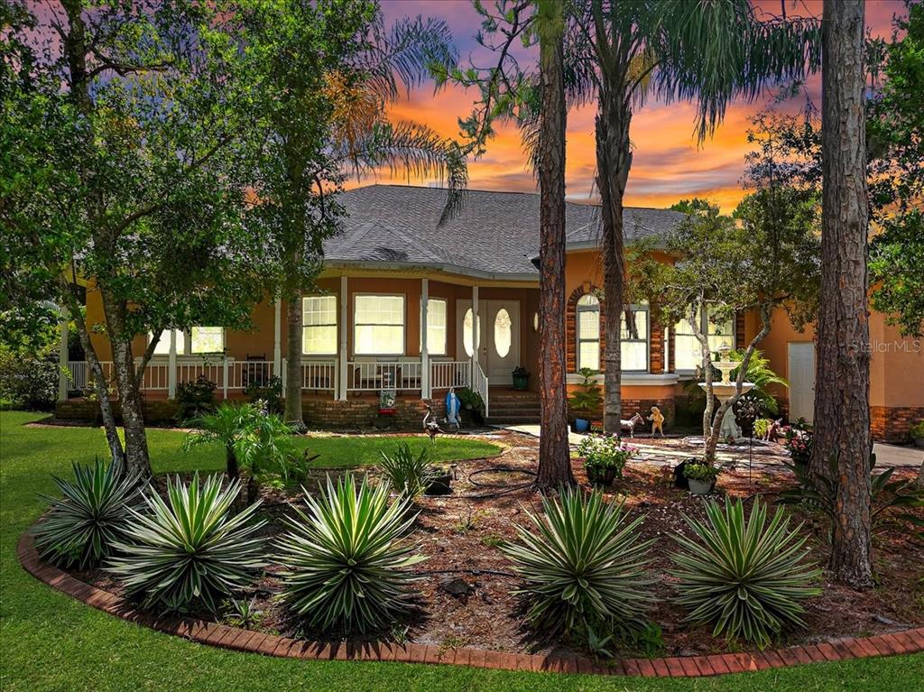 A single-story house with a covered porch and landscaped yard under a sunset sky — 1727 STREAM AVENUE, SEBRING, FL