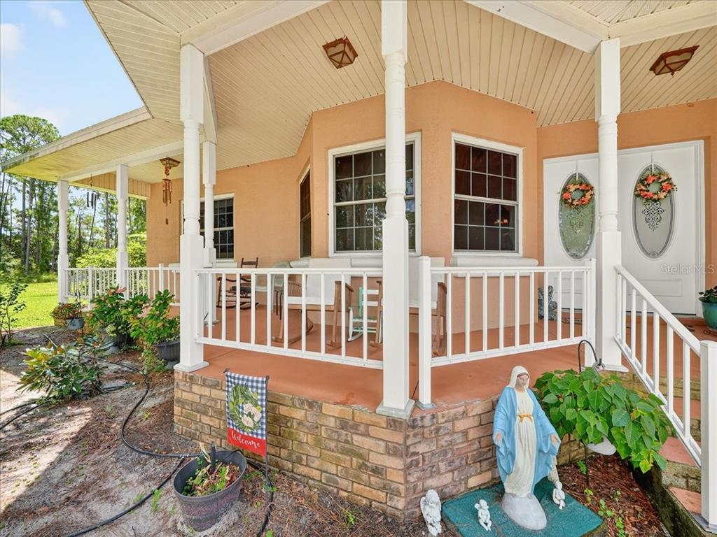A covered porch with a brick base, white railings, and a statue of the Virgin Mary — 1727 STREAM AVENUE, SEBRING, FL