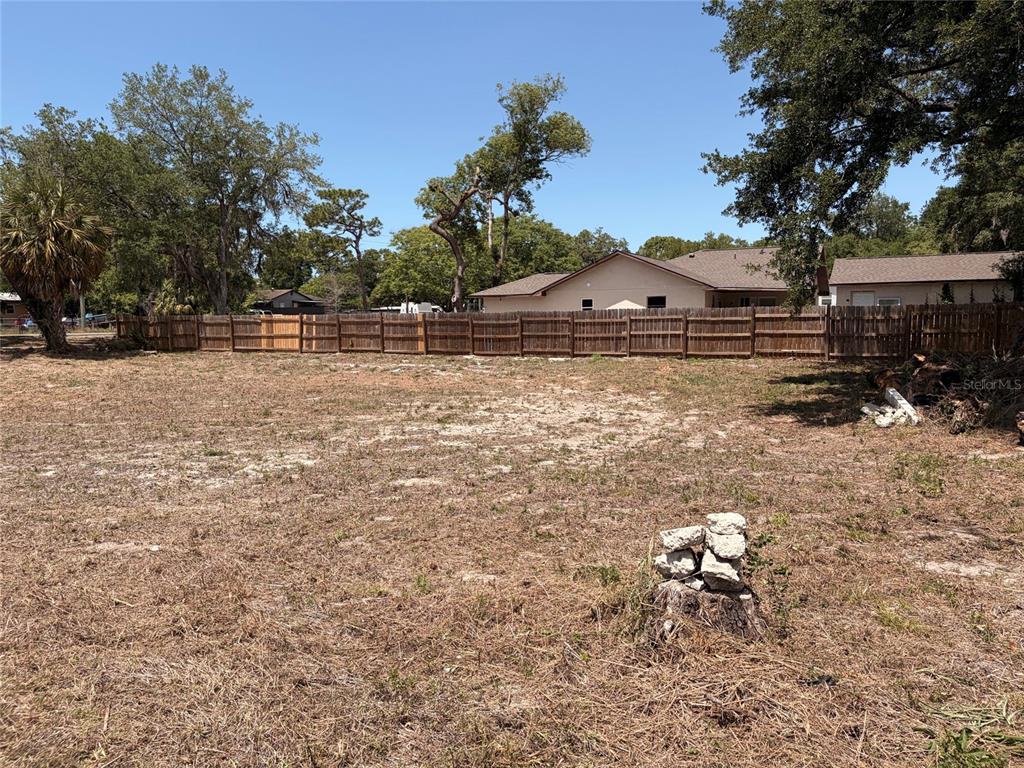 A large, cleared, grassy lot features a wooden fence and mature trees in the background — HICKS ROAD, HUDSON, FL