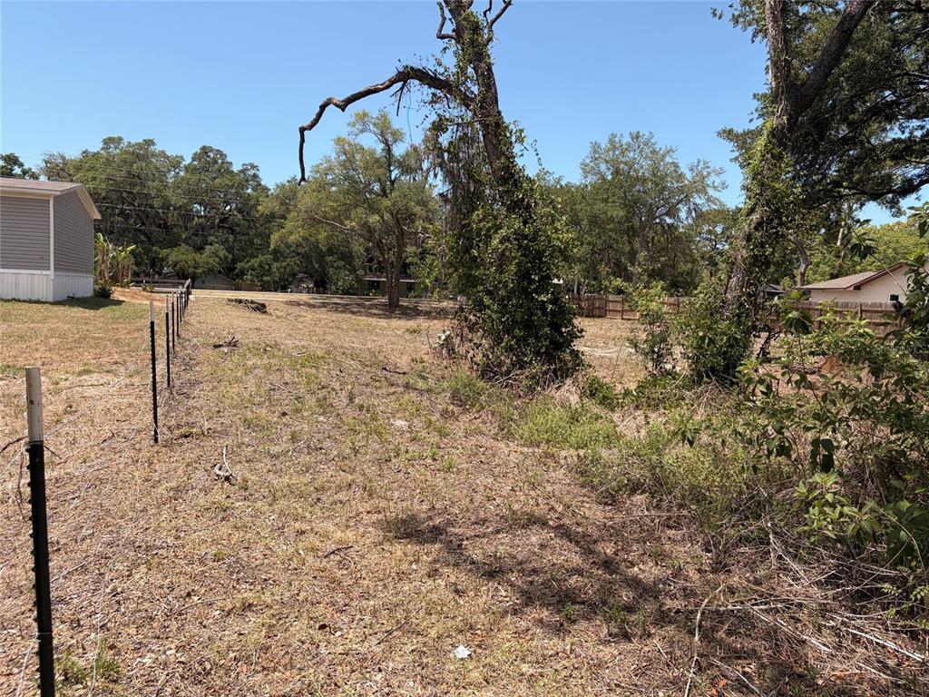A grassy, partially wooded vacant lot features a wire fence and a neighboring house — HICKS ROAD, HUDSON, FL