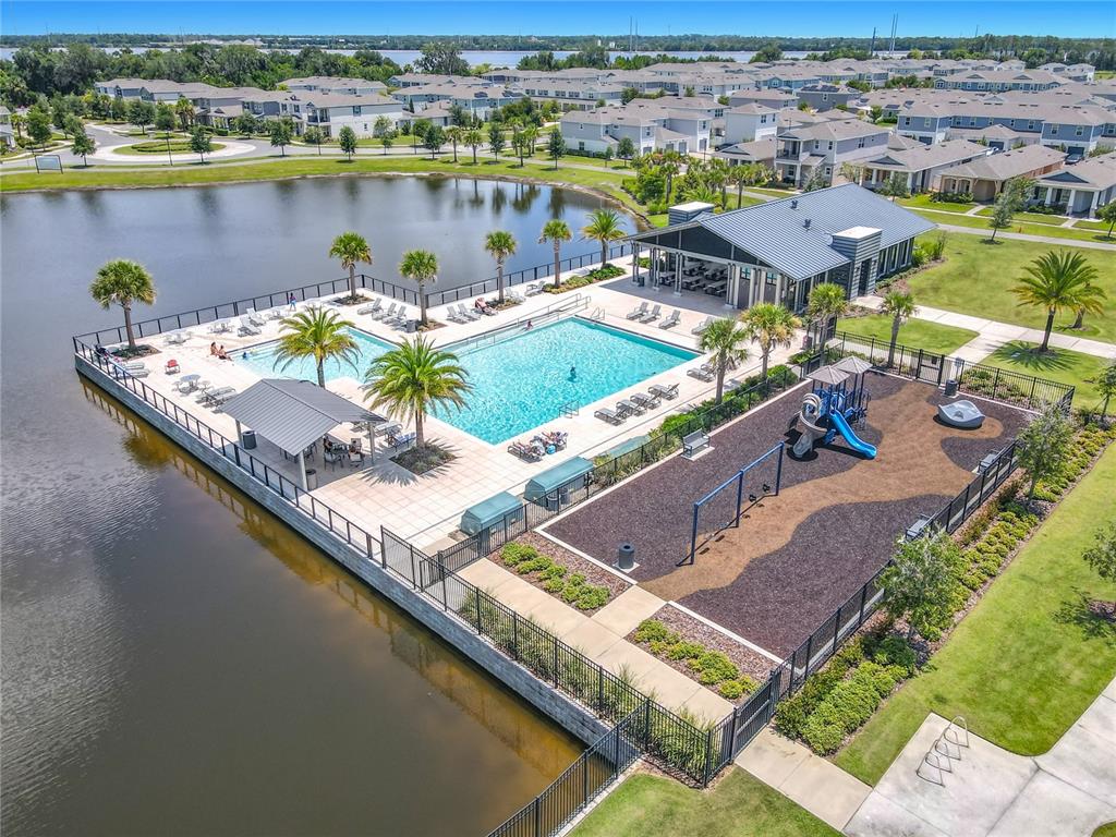 An aerial view shows a community swimming pool and playground situated next to a lake — 720 TREEHOUSE LOOP, DEBARY, FL