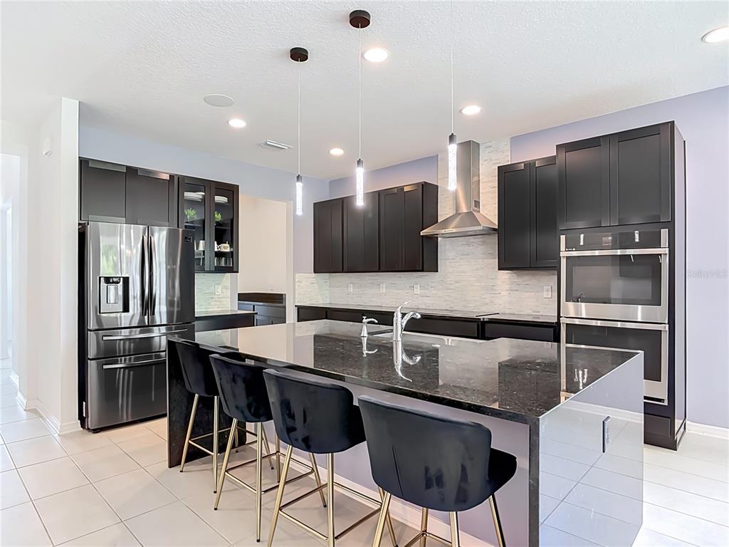 A modern kitchen features dark cabinetry, a large granite island with bar seating, and stainless appliances — 720 TREEHOUSE LOOP, DEBARY, FL