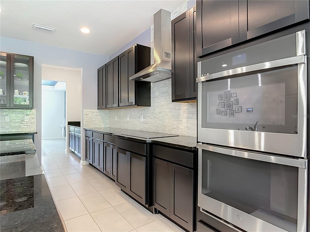 A kitchen features dark cabinetry, stainless steel appliances, a tiled backsplash, and light-colored floor tiles — 720 TREEHOUSE LOOP, DEBARY, FL