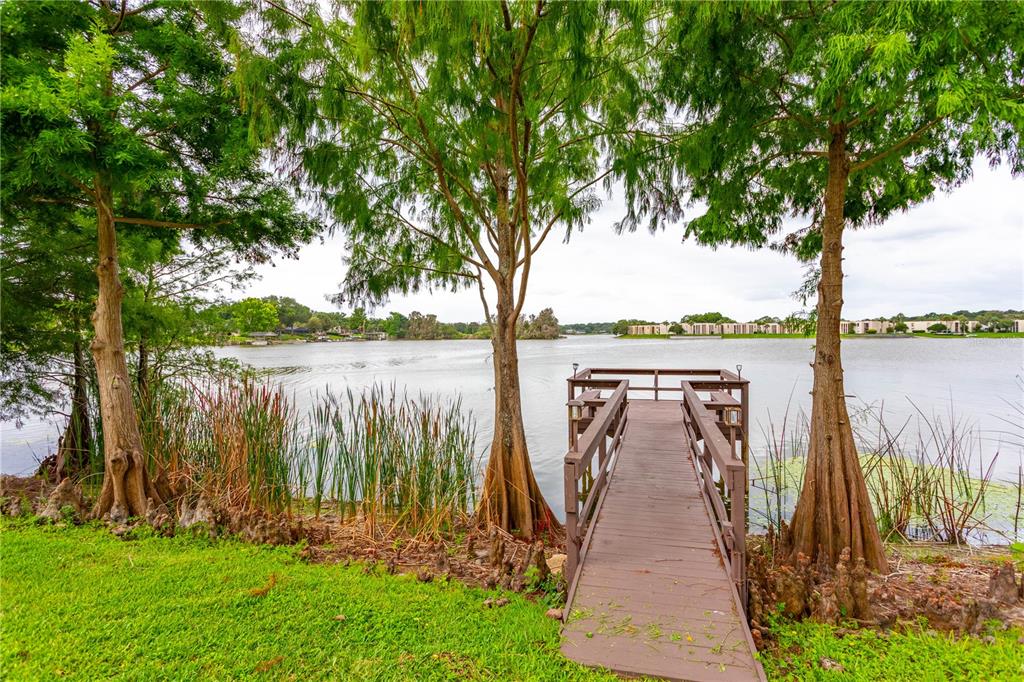 A wooden dock extends from a grassy shore into a lake framed by cypress trees — 618 ORANGE DRIVE UNIT 216, ALTAMONTE SPRINGS, FL