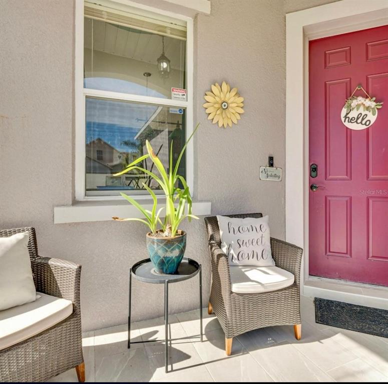 A covered front porch features two wicker chairs, a small side table with a plant, and a red door — 345 SONJA CIRCLE, DAVENPORT, FL