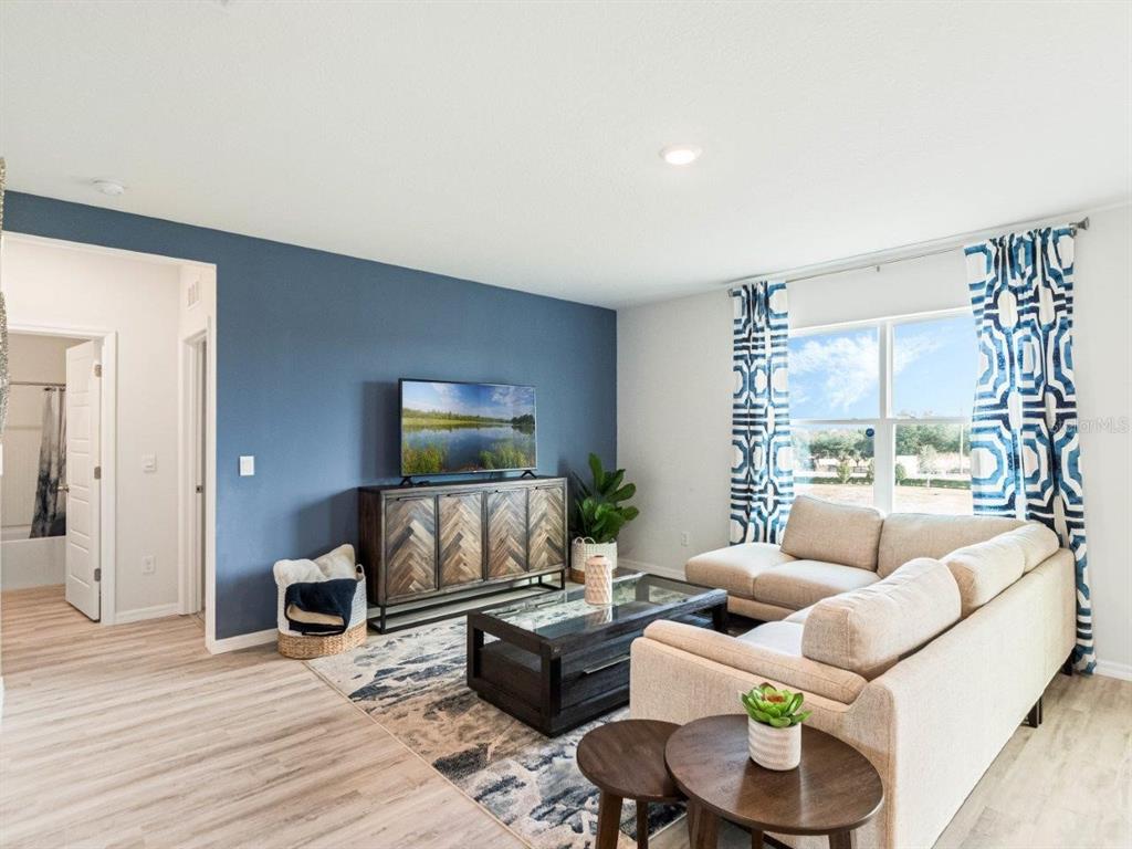 A living room features a blue accent wall, a sectional sofa, and a patterned rug — 2482 AVEENO AVENUE, HAINES CITY, FL