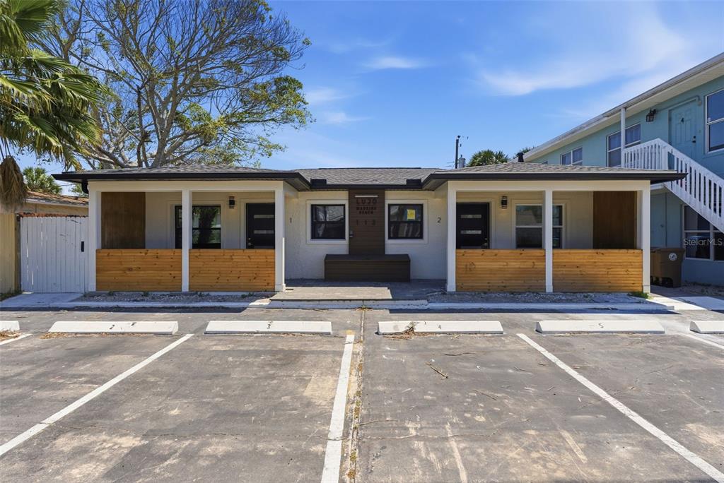 A single-story building with two covered porches, wood-slat railings, and a paved parking lot — 113 145TH AVENUE E UNIT 5, MADEIRA BEACH, FL