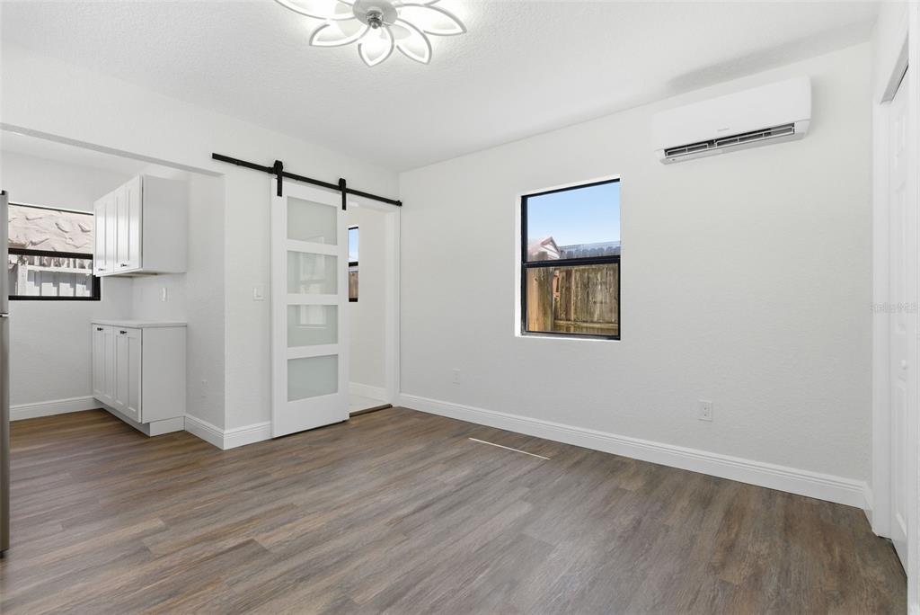 A room with wood-look flooring, a sliding barn door, a window, and a wall-mounted AC unit — 113 145TH AVENUE E UNIT 5, MADEIRA BEACH, FL