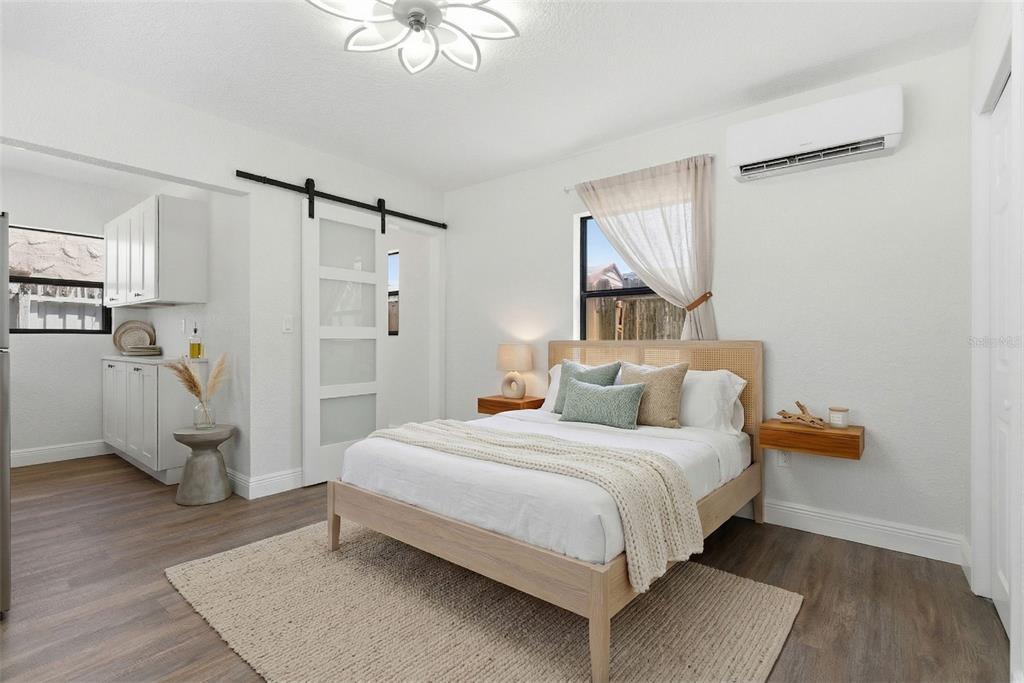 A bedroom features a light wood bed frame, a sliding barn door, and white cabinetry — 113 145TH AVENUE E UNIT 5, MADEIRA BEACH, FL