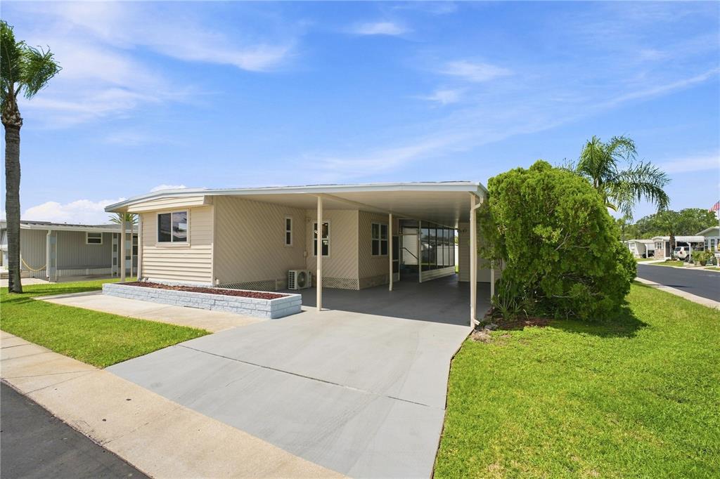 A beige mobile home features a concrete driveway, a carport, and a small front garden — 10929 TIOGA DRIVE, PORT RICHEY, FL