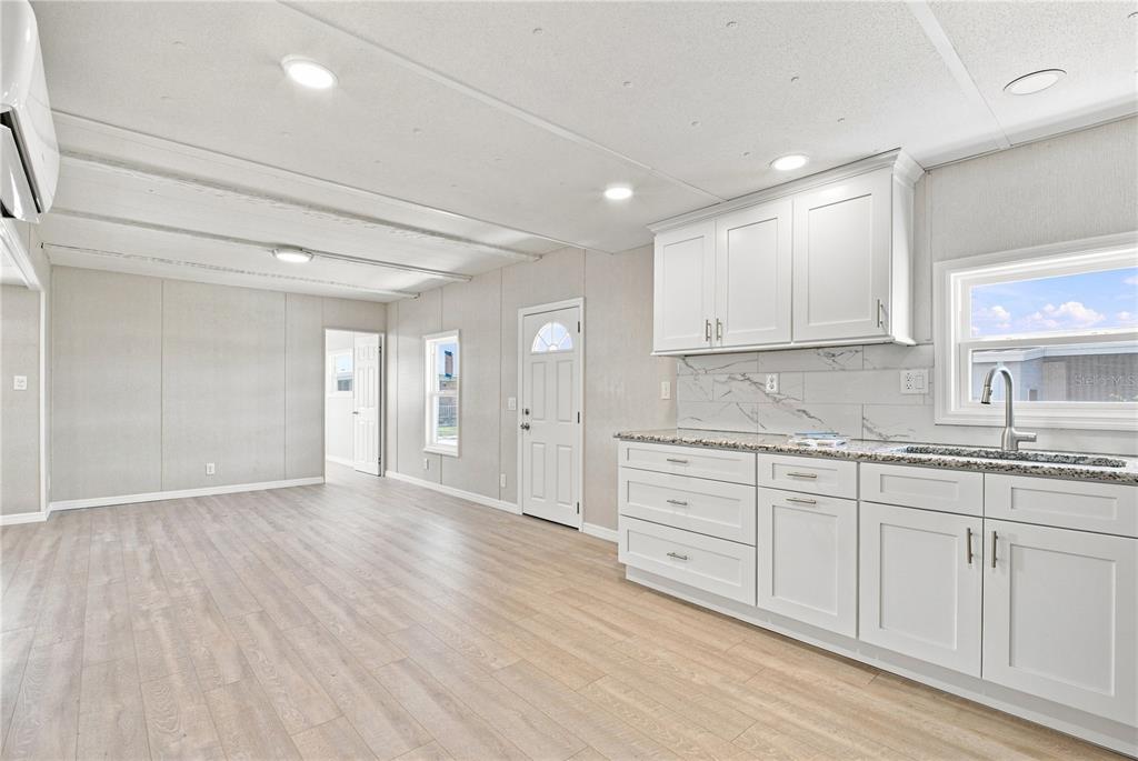 A kitchen with white cabinets and a marble-style backsplash opens into a living area — 10929 TIOGA DRIVE, PORT RICHEY, FL