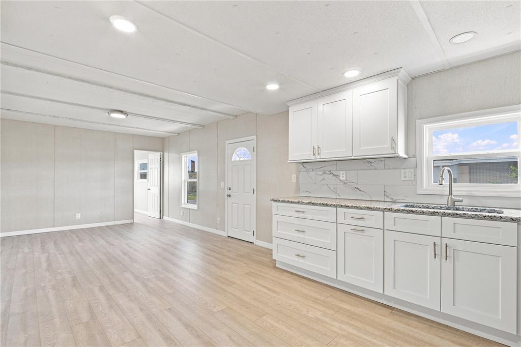 A kitchen with white cabinets, granite countertops, and light wood flooring in an open room — 10929 TIOGA DRIVE, PORT RICHEY, FL