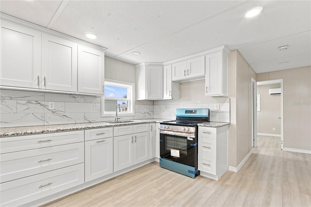 A kitchen with white cabinets, granite countertops, a marble-look backsplash, and a new black stove — 10929 TIOGA DRIVE, PORT RICHEY, FL