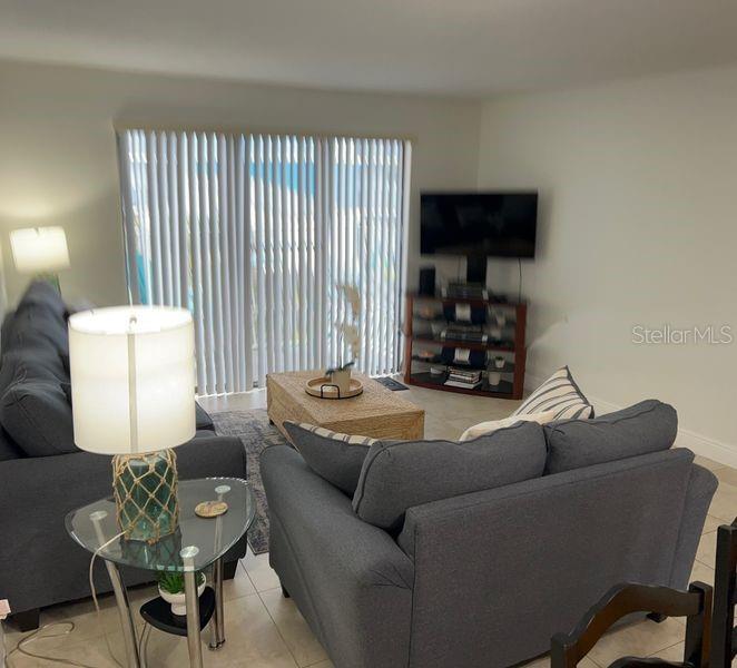 A living room features gray sofas, a glass side table, and a television on a stand — 5350 OCEAN BEACH BOULEVARD UNIT 210, COCOA BEACH, FL