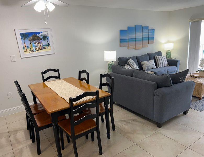 A dining area with a wooden table and chairs sits beside a living room sofa — 5350 OCEAN BEACH BOULEVARD UNIT 210, COCOA BEACH, FL