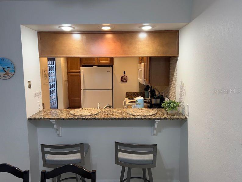 A kitchen pass-through window features a granite breakfast bar with two stools below — 5350 OCEAN BEACH BOULEVARD UNIT 210, COCOA BEACH, FL