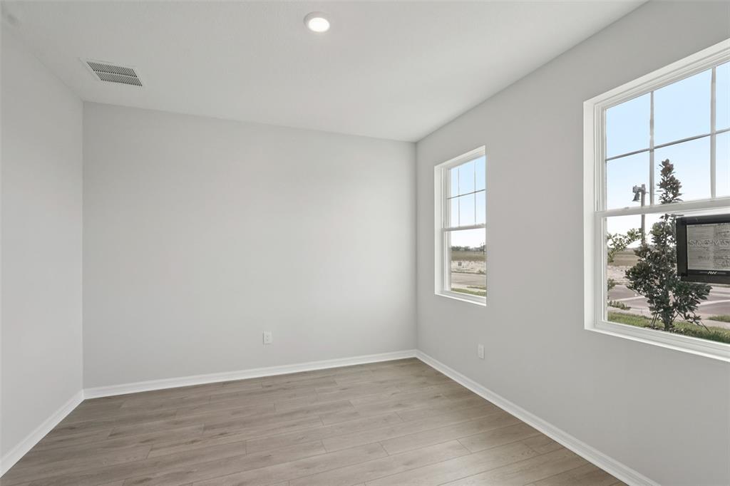 An empty room with light gray walls, wood-look flooring, and two windows overlooking a street — 2909 CITRUS GROVE STREET, WIMAUMA, FL