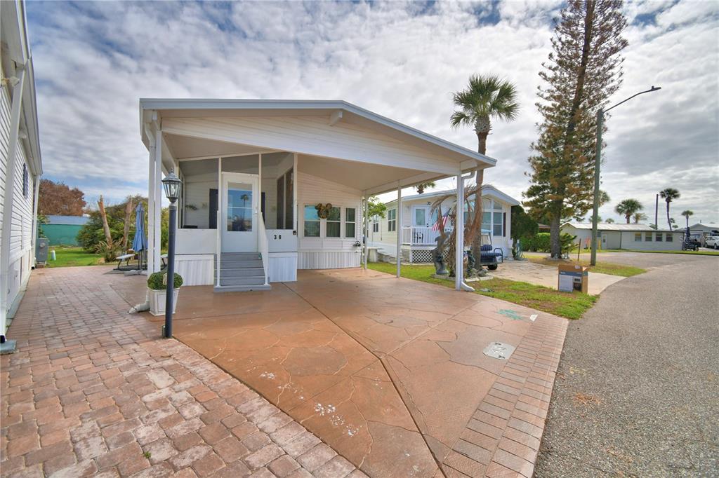 A mobile home with a screened porch, carport, and paved driveway under a cloudy sky — 9000 US HIGHWAY 192 UNIT 38, CLERMONT, FL