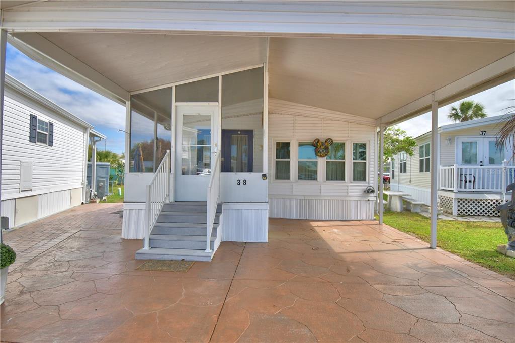 A mobile home exterior features a screened-in porch, a covered carport, and concrete flooring — 9000 US HIGHWAY 192 UNIT 38, CLERMONT, FL