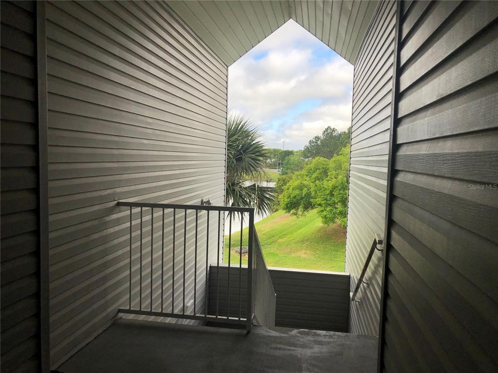 An outdoor stairwell with gray siding leads down toward a view of trees and grass — 717 SECRET HARBOR LANE UNIT 313, LAKE MARY, FL