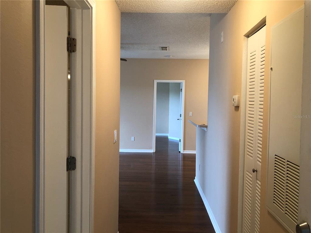 A hallway with wood flooring leads to a living area with a doorway beyond — 717 SECRET HARBOR LANE UNIT 313, LAKE MARY, FL