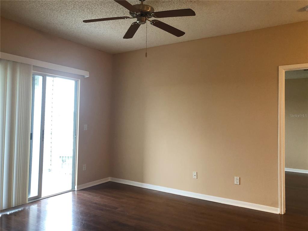 A room with dark wood flooring, beige walls, a ceiling fan, and a sliding glass door — 717 SECRET HARBOR LANE UNIT 313, LAKE MARY, FL