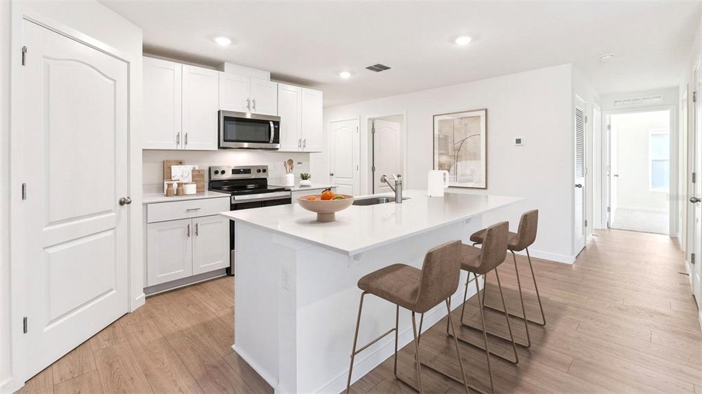 A modern kitchen features white cabinetry, a central island with bar seating, and light flooring — 133 HEIRLOOM DRIVE, ORMOND BEACH, FL