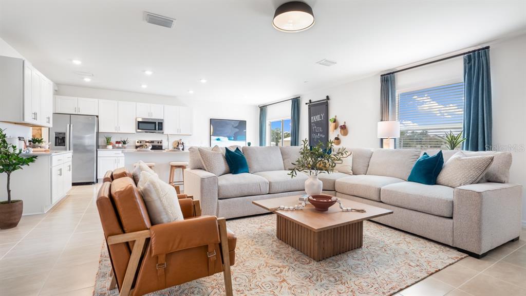 A bright open-concept living room features a large sectional sofa, leather armchairs, and a kitchen — 13741 SQUALL LANE, HUDSON, FL