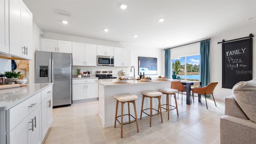 A modern kitchen features white cabinetry, stainless steel appliances, a central island, and dining area — 13741 SQUALL LANE, HUDSON, FL