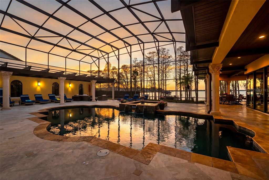 A screened-in pool area features a stone-tiled deck, a hot tub, and sunset lake views — 5070 DOWN POINT LANE, WINDERMERE, FL