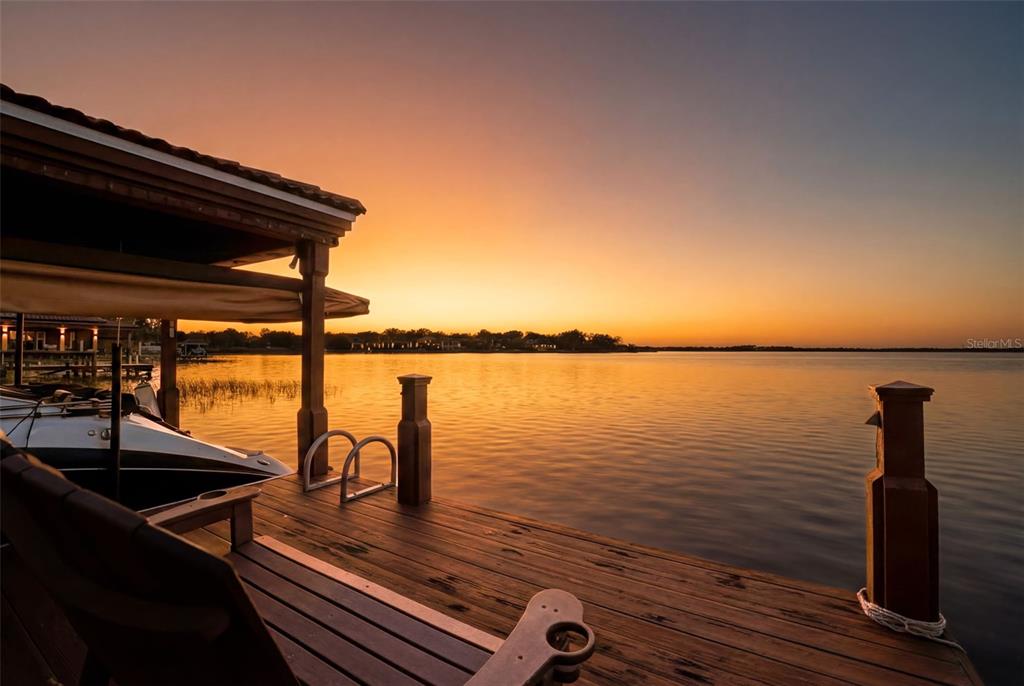 A wooden boat dock with a covered slip overlooks a lake at sunset — 5070 DOWN POINT LANE, WINDERMERE, FL