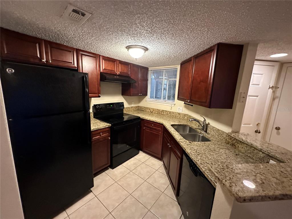 A kitchen features dark wood cabinets, granite countertops, a black refrigerator, and tile flooring — 1940 LAKE ATRIUMS CIRCLE UNIT 89, ORLANDO, FL