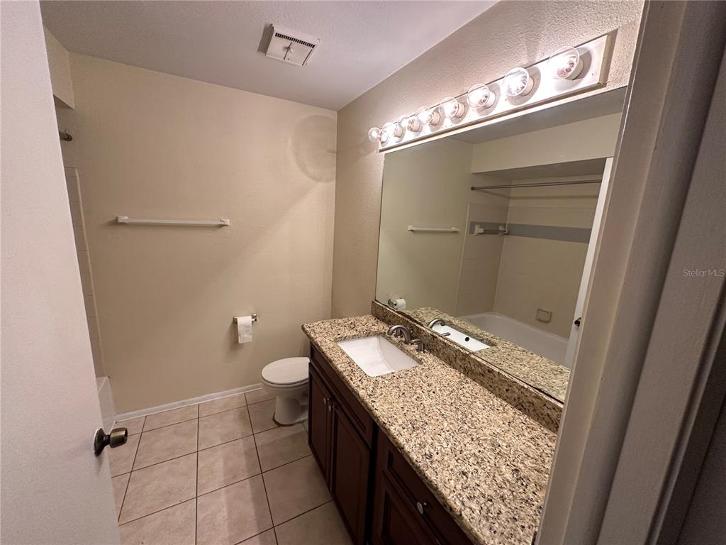A bathroom features a granite-topped vanity, dark wood cabinets, a large mirror, and tiled flooring — 1940 LAKE ATRIUMS CIRCLE UNIT 89, ORLANDO, FL