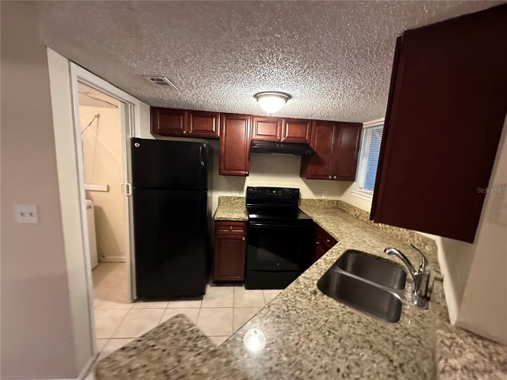 A kitchen features dark wood cabinets, black appliances, and granite countertops — 1940 LAKE ATRIUMS CIRCLE UNIT 89, ORLANDO, FL