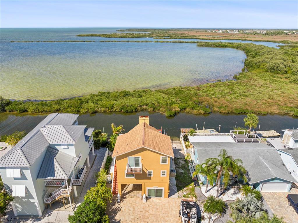 An aerial view shows a yellow house situated between a canal and a large bay — 6633 DRIFTWOOD DRIVE, HUDSON, FL