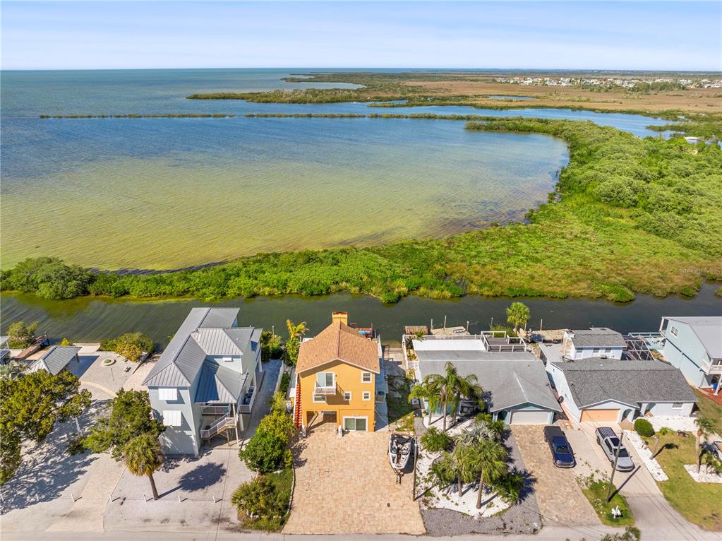 An aerial view shows a yellow house with a paved driveway facing a coastal waterway — 6633 DRIFTWOOD DRIVE, HUDSON, FL